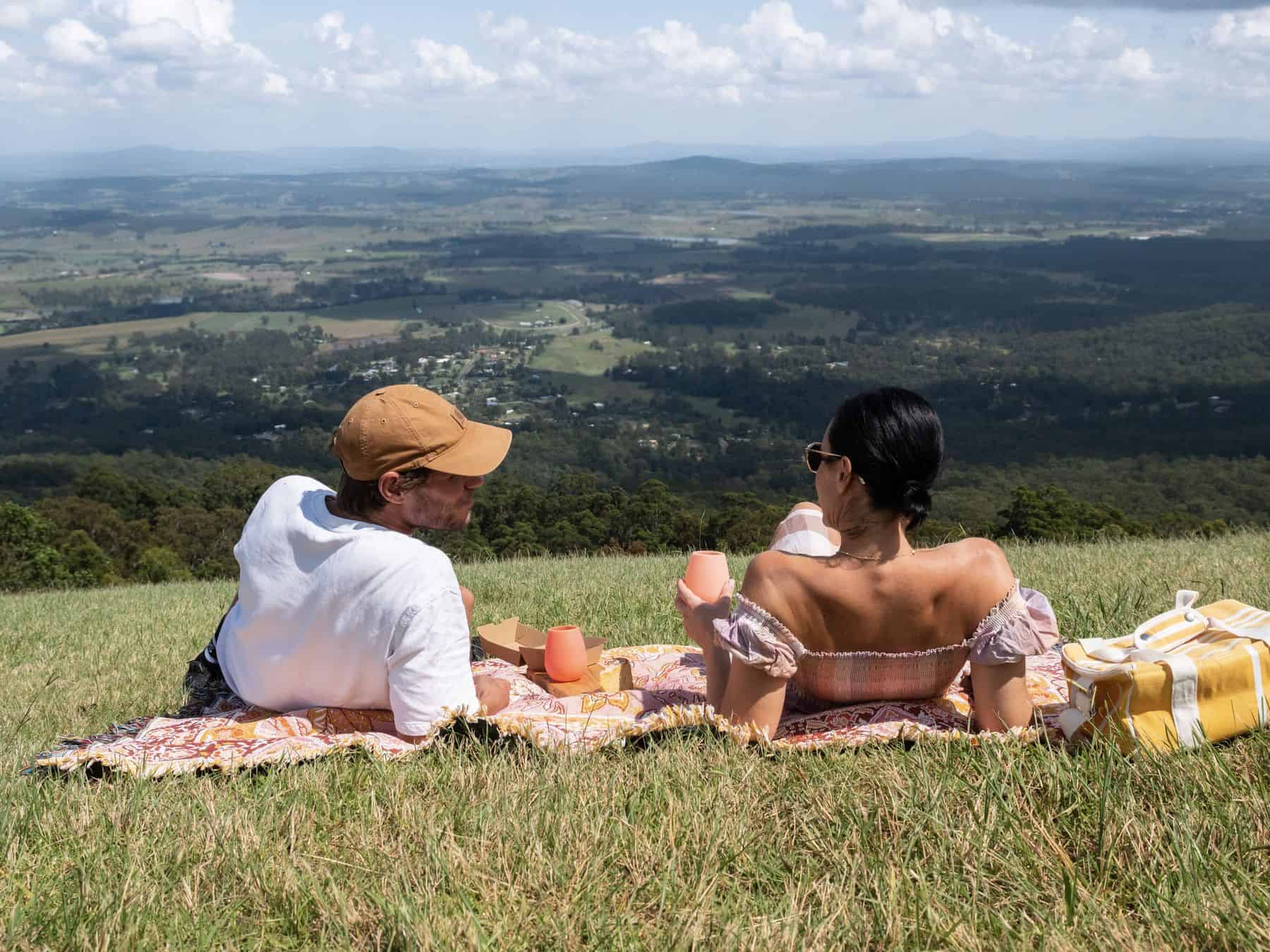 Two people having a picnic on the grass with views over the valley from Tamborine Mountain